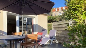 Une terrasse extérieure avec une table et des chaises, un grand parasol et une plante en pot.