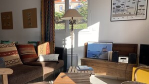 Un salon avec un canapé, une table basse en bois, un téléviseur et une fenêtre avec des rideaux.