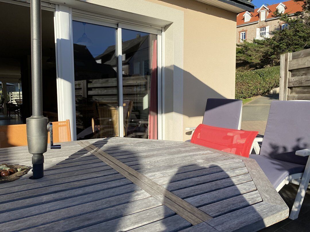 Une terrasse en bois avec une table et des chaises, une fontaine et une porte-fenêtre coulissante donnant sur un espace abrité.