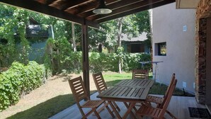 Eine Terrasse im Freien mit einem Holztisch und -stühlen, umgeben von einem Garten und einem Gebäude.
