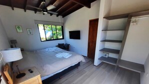 Ein Schlafzimmer mit Bett, Nachttisch, Lampe, Fernseher, Fenster, Tür und integriertem Regal.