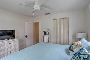 Ein Schlafzimmer mit Bett, Kommode, Fernseher, Kleiderschrank, Spiegel und Deckenventilator.