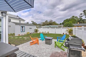 Ein Garten mit einer Terrassenfläche, ausgestattet mit bunten Adirondack-Stühlen, einem Grill und einem kleinen Tisch.