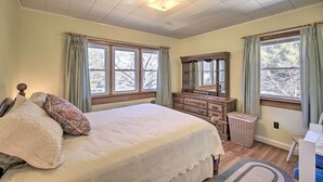 Un dormitorio con una cama grande, un aparador, un espejo y dos ventanas con cortinas.