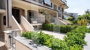A multi-story residential building with a covered outdoor area, steps leading to the entrance, and a landscaped garden.