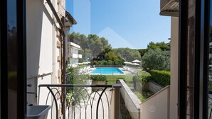 A balcony with a view of a swimming pool, surrounded by greenery and other buildings.
