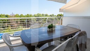 Un balcón con mesa y sillas, una planta en maceta y vista a zonas verdes.