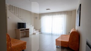 Un salón amplio con una escalera, un televisor de pantalla plana y dos sofás tapizados en color naranja.