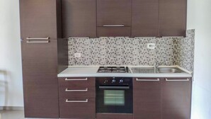 A compact kitchen with dark brown cabinets, a tiled backsplash, a gas stove, a sink, and a built-in oven.