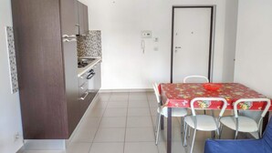A compact kitchen with modern appliances, a dining table with chairs, and a door.