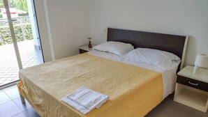A hotel room with a bed, a nightstand, a lamp, and a view of the outside.