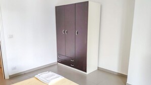 A room with a large wardrobe, a bed with a white bedspread, and a light-colored floor.