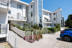 Un immeuble résidentiel moderne à plusieurs étages, doté de balcons, d’une allée pavée et d’un abri à vélos.