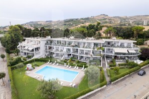 A hotel with a swimming pool, multiple balconies, and a view of the surrounding landscape.