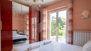 Une chambre à coucher comprenant un lit, une armoire, un miroir, une fenêtre avec des rideaux et une vue sur la verdure.