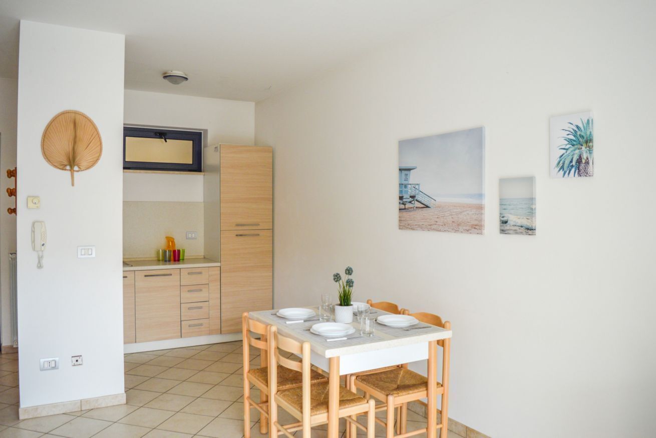 Una cucina compatta con mobili in legno, un tavolo da pranzo per quattro persone e un'opera d'arte a tema spiaggia.