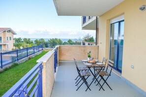 A balcony with a table and chairs, overlooking a coastal area.