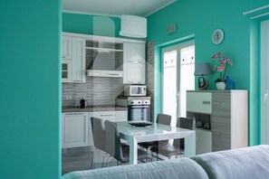 Une cuisine moderne avec des meubles blancs, un four à micro-ondes et une cuisinière. On aperçoit une table à manger avec des chaises et un canapé au premier plan.