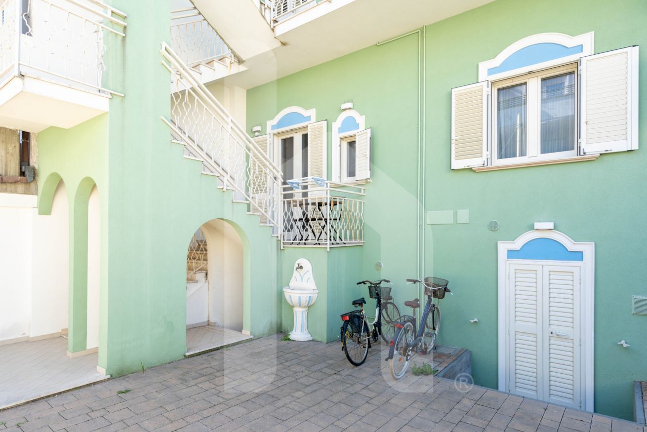 Un bâtiment à la façade verdoyante, avec une porte blanche et un escalier menant à un balcon.