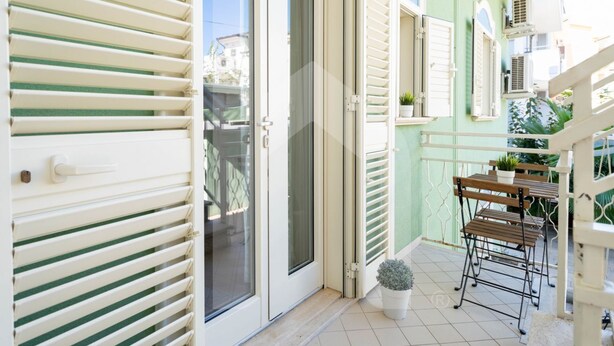 Een balkon met een tafel, stoelen, een bloempot en een schuifdeur.
