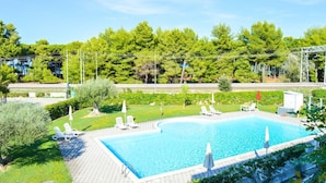 Une piscine rectangulaire, bordée d’une terrasse carrelée et entourée de verdure et d’arbres.