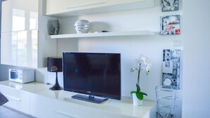 Un salon moderne avec un téléviseur à écran plat, un meuble blanc, des vases décoratifs et des œuvres d’art murales.