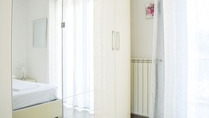 Une chambre à coucher comprenant un lit, une armoire, un radiateur et une fenêtre avec des rideaux légers.
