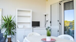 Un espace repas comprenant une table, des chaises, un téléviseur posé sur une étagère et des plantes en pot.