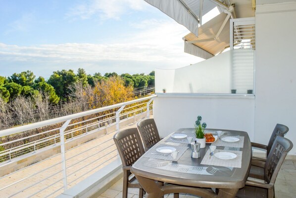 Un espace de restauration en plein air avec une table dressée pour quatre personnes, entourée de chaises, offrant une vue panoramique sur un paysage arboré et un ciel dégagé.