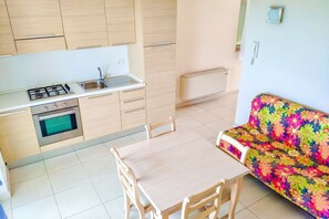 Une cuisine compacte équipée d’une cuisinière à gaz, d’un four et d’un évier. On y trouve une table à manger avec des chaises et un canapé coloré.