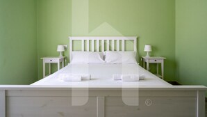 A neatly made bed with white bedding and pillows, two bedside tables with lamps, and green walls.