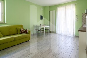 Una sala de estar con un sofá verde, una mesa de comedor con sillas y una zona de cocina.