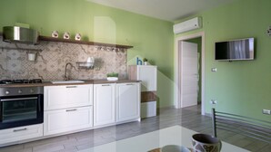 A modern kitchen with white cabinets, a gas stove, and a built-in oven. There is a sink, a microwave, and a small refrigerator. The walls are painted green, and there is a TV mounted on the wall.