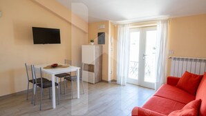 A compact living space with a dining area, a red sofa, a TV mounted on the wall, and a sliding glass door leading to a balcony. - D'Annunzio Residence - Sedna - Apartment a stone's throw from the sea (Pineto)