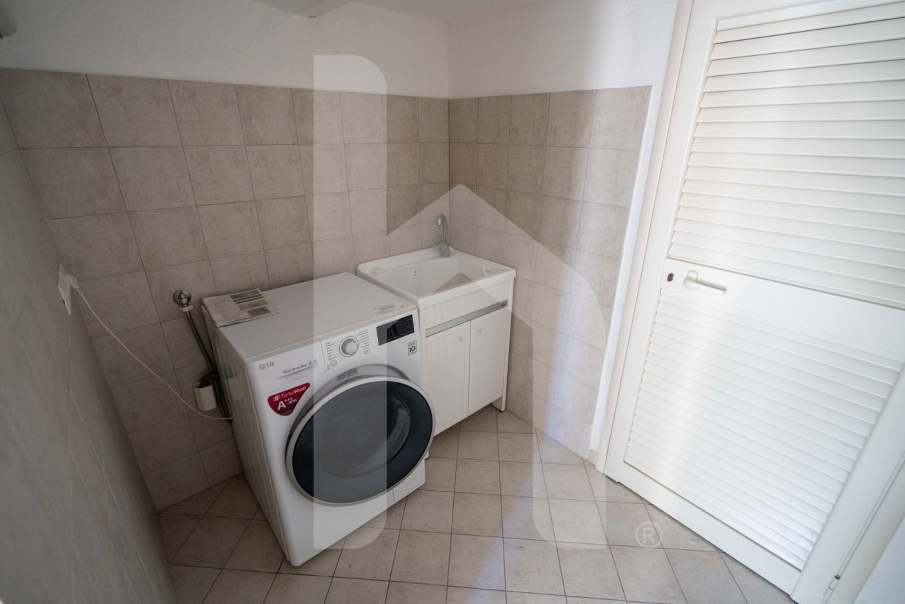 A compact laundry room with a washing machine and a sink, tiled walls, and a white door.