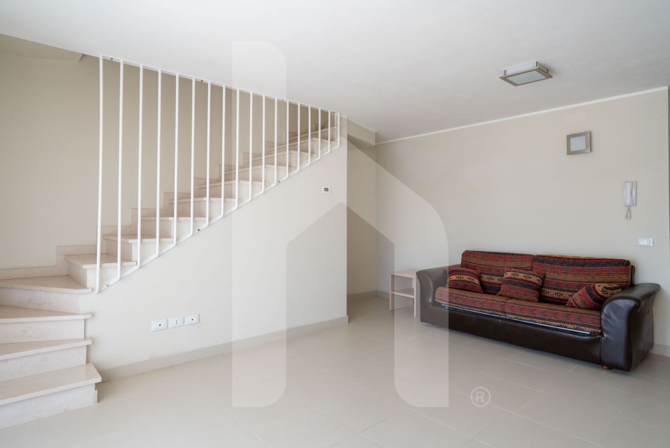 A staircase with white railings leading to an upper floor, a sofa with patterned cushions, and a small table.