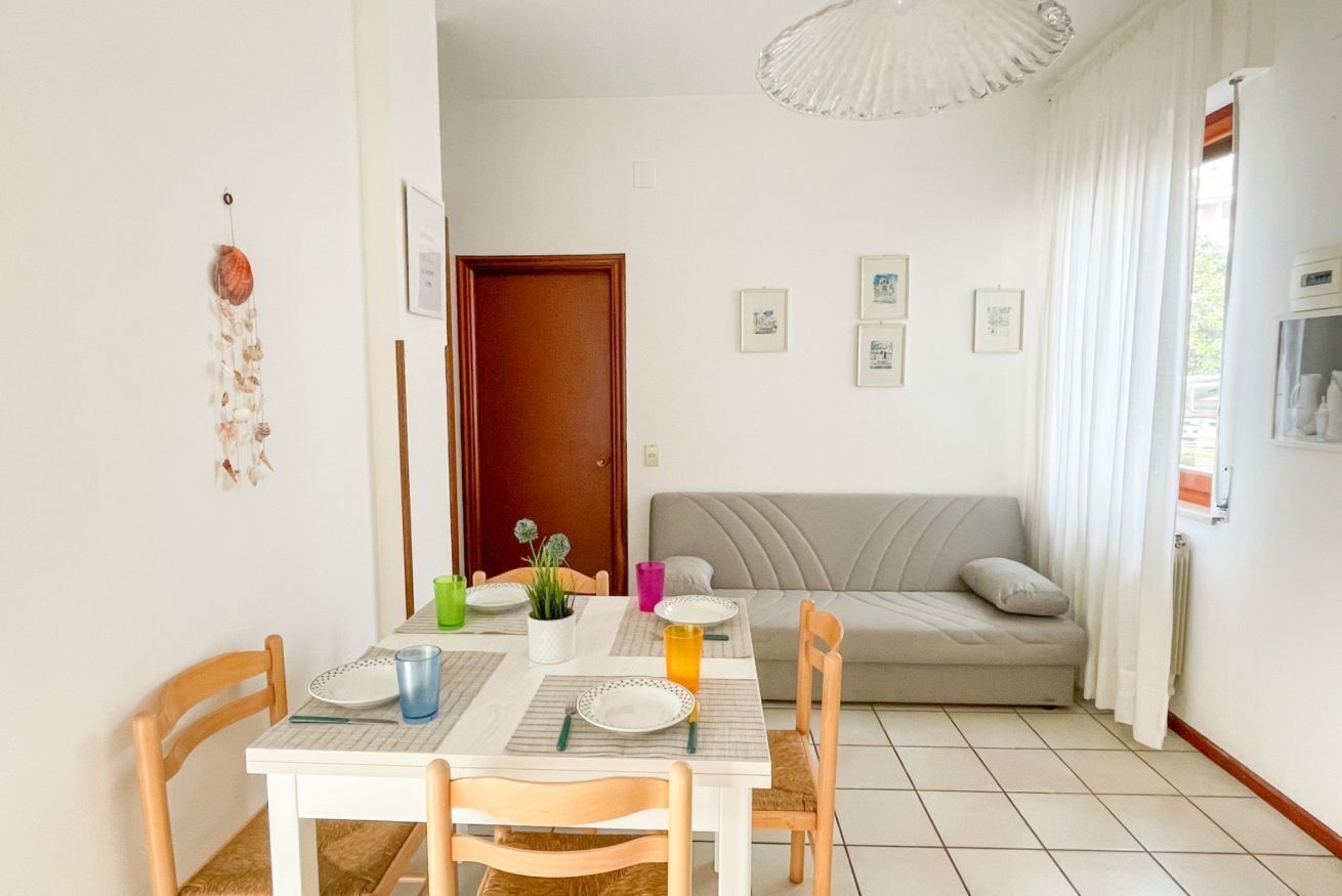 A dining area with a table set for four, a sofa, and a dreamcatcher on the wall.