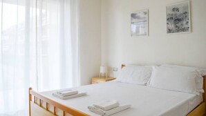 Un lit bien fait, avec du linge de lit et des serviettes blanches, une table de chevet avec une lampe, et deux œuvres d’art encadrées accrochées au mur.