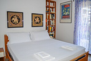Una cama bien hecha con ropa blanca, un cabecero de madera y una estantería con libros y adornos.