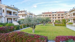 A courtyard with a lawn, a tree, and a row of buildings with balconies. - Micaene D05 - Perseo - First floor apartment with balcony (Pineto)