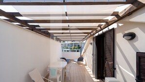 A covered outdoor patio with a table and chairs, a view of the street, and a building entrance.
