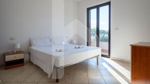 A bedroom with a bed, a nightstand, a desk, and a sliding glass door to a balcony.
