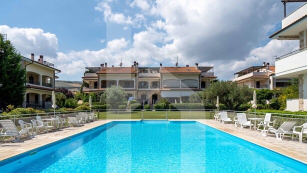A swimming pool with lounge chairs, surrounded by buildings with balconies and a clear sky.