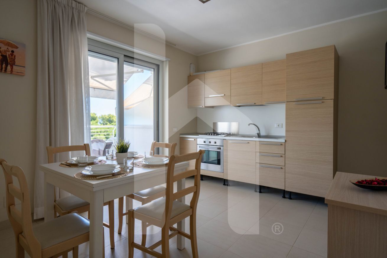 A modern kitchen with light wood cabinets, a built-in oven, and a dining area with a table set for four.