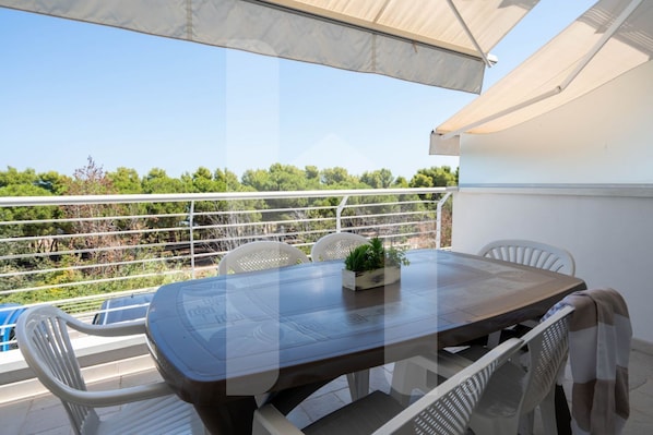 A balcony with a table and chairs, a potted plant, and a view of greenery.