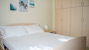 Una cama bien hecha con sábanas blancas, un cabecero de madera y una mesita de noche con una lámpara.