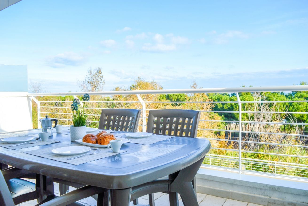 Un balcon avec une table dressée pour deux personnes, agrémentée d’une cafetière, d’assiettes et d’une plante.