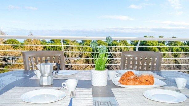 Une table mise pour le petit-déjeuner, avec des croissants, une cafetière et une plante en pot.
