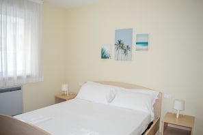 A hotel room with a bed, a nightstand, a lamp, and wall art depicting palm trees and a beach scene.