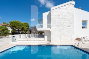 A modern building with a swimming pool, white exterior, and a clear blue sky.
